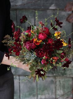 a woman holding a bouquet of flowers in her hand with red, yellow and orange colors