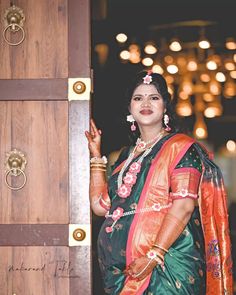 a woman standing in front of a wooden door wearing a green and orange sari