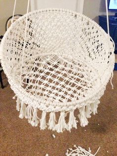 a white hanging chair with tassels on the floor next to a laptop computer