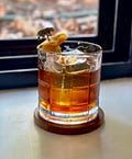 a glass filled with liquid sitting on top of a wooden table next to a window