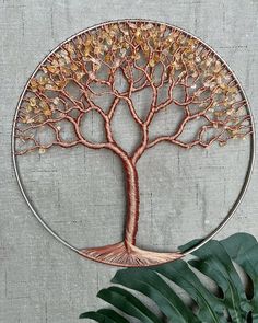 a metal wall hanging with a tree in the center and leaves around it on a gray background