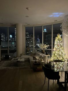 a living room filled with furniture and a christmas tree in front of large windows at night