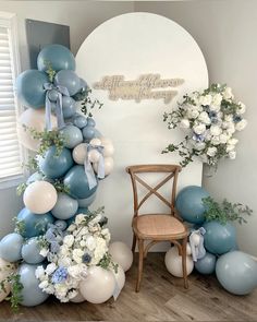 a chair sitting in front of a balloon arch with flowers and balloons on the wall