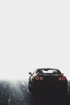 a black sports car driving down a road in the rain with its headlights turned on