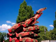 a pile of red cars sitting in the middle of a parking lot next to trees