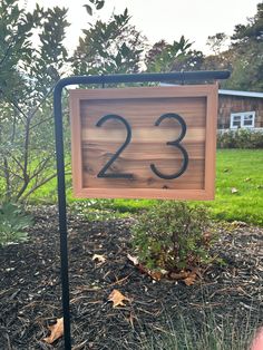 a wooden sign with the number twenty three on it in front of some grass and trees