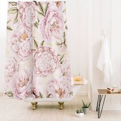 a shower curtain with pink flowers on it next to a white bath tub and wooden floor