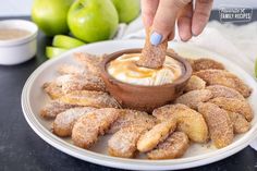 a person dipping something into a small bowl on top of some sugared donuts