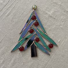 a stained glass christmas tree ornament hanging on a white surface with red beads