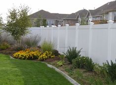 a white fence in front of houses with flowers and plants growing on the side walk