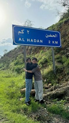 two people standing in front of a road sign