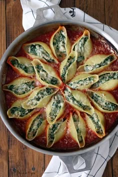 a pan filled with ravioli and spinach on top of a wooden table next to napkins