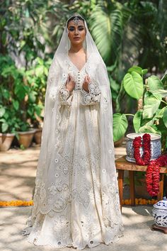 a woman in a white wedding gown and veil with flowers on the ground next to potted plants