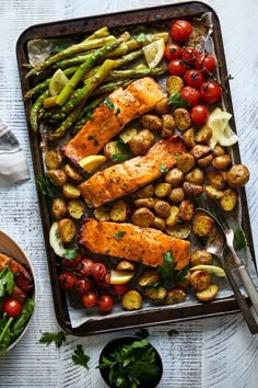 salmon, potatoes and asparagus on a sheet pan with spoons next to it