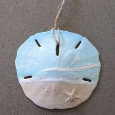 a ceramic ornament hanging from a rope on the floor with sand and starfish