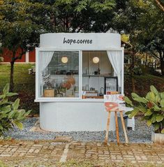 a small white shop sitting in the middle of a park with lots of greenery