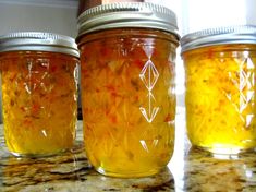 three jars filled with yellow liquid sitting on top of a marble counter next to a window