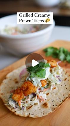 a wooden cutting board topped with a tortilla covered in shrimp