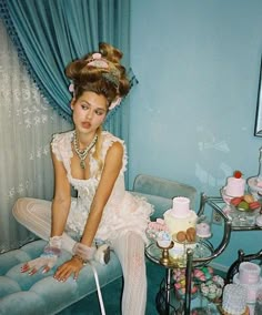 a woman sitting on top of a couch next to a table filled with cakes and cupcakes