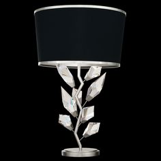 a table lamp with a black shade on it's side and leaves attached to the base