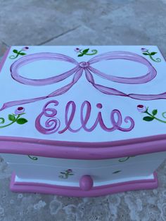 a pink and white box with a bow on the lid that says,'ellie '