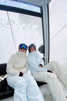 two people sitting on top of a ski lift in the snow with their arms around each other