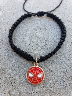 a necklace with a spider - man pendant on it sitting on a stone surface next to a black cord