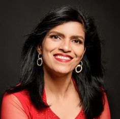 a woman with long black hair and earrings smiling at the camera, wearing a red top