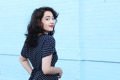 a woman standing in front of a blue wall wearing a black and white polka dot dress