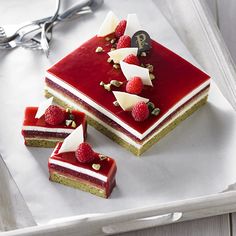 three pieces of cake with raspberry toppings on a white tray next to silver utensils