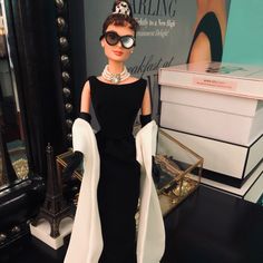 a barbie doll dressed in a black and white dress with sunglasses on her head, standing next to a jewelry box