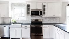 a white kitchen with black counter tops and stainless steel dishwasher in the center