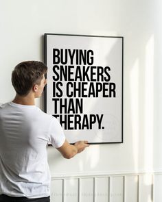 a man is pointing to a poster with words on it that say buying sneakers is cheaper than therapy