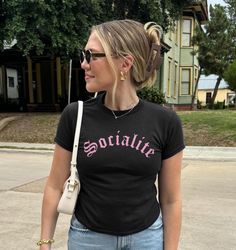 a woman in black shirt and jeans holding a white handbag walking down the street