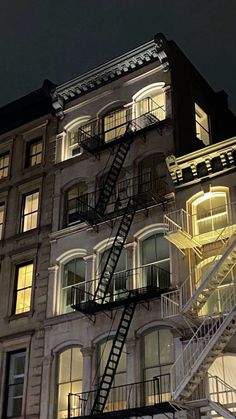 a fire escape is lit up at night in front of an apartment building with stairs leading to the upper floor