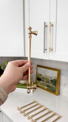 a person is holding a golden handle on a white counter top in a kitchen with gold hardware