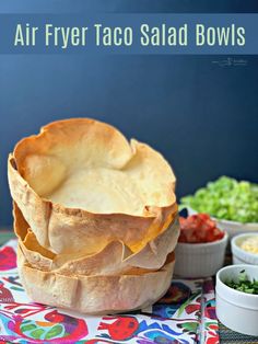 an air fryer taco salad bowl on a colorful table cloth with bowls of vegetables in the background