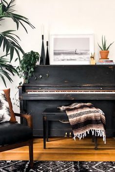 a black piano in a living room next to two chairs and a potted plant