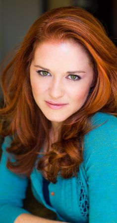 a woman with red hair and green eyes is sitting in front of a window looking at the camera