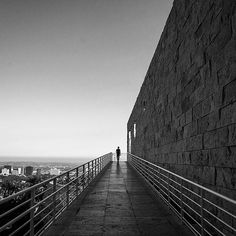 a person walking down a walkway next to a stone wall with metal handrails