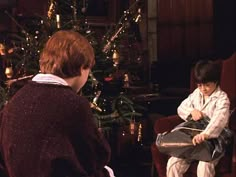 two people sitting in chairs near a christmas tree and one person is holding a piece of paper