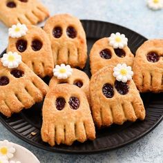 some cookies with jelly in the shape of hands and flowers on a black plate next to white daisies