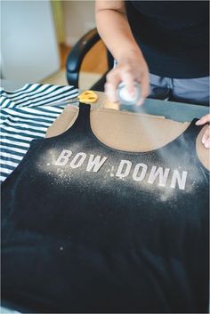 a person cutting up a black shirt with the words bow down on it and gold buttons