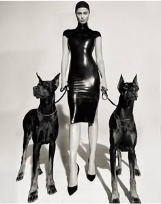 a woman in a leather dress with two dogs on leashes standing next to each other