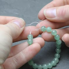 two hands are holding green beads and threading them together to make a beaded bracelet