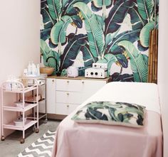 a bed room with a neatly made bed next to a wallpapered plant mural