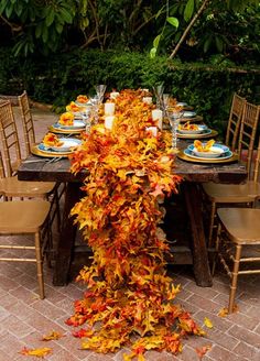 the table is set with plates and place settings covered in fall leaves, along with candles