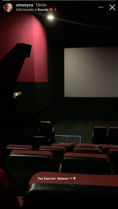 an empty movie theater with red walls and black seats, the screen is lit up