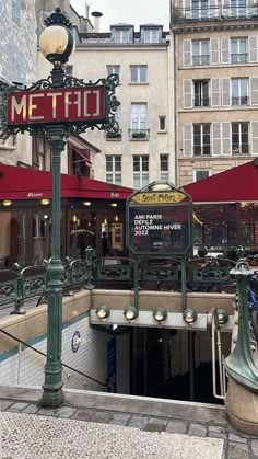 a sign that is on the side of a pole in front of some buildings with red awnings