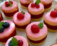 small pastries with pink icing and raspberries on top are sitting on a plate